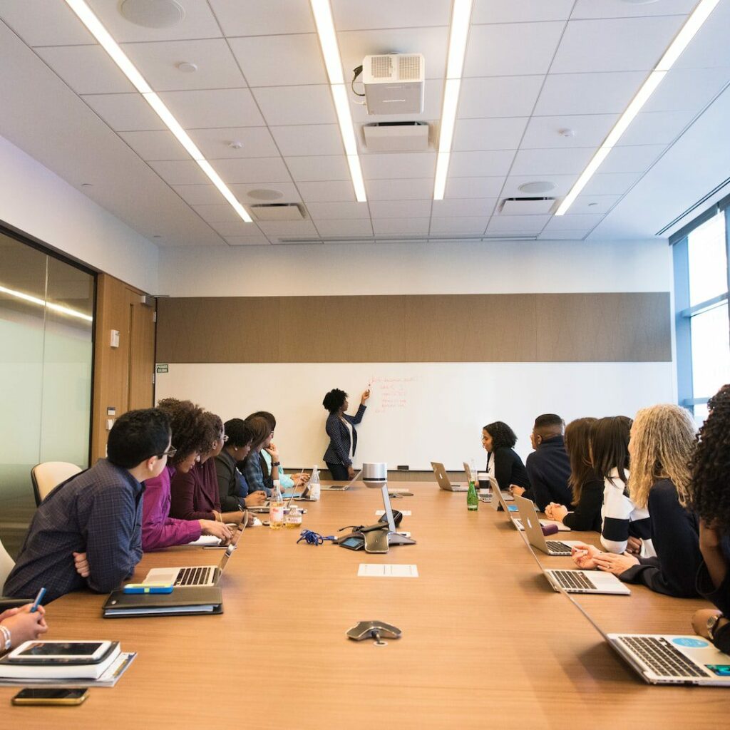 people on conference table looking at talking woman