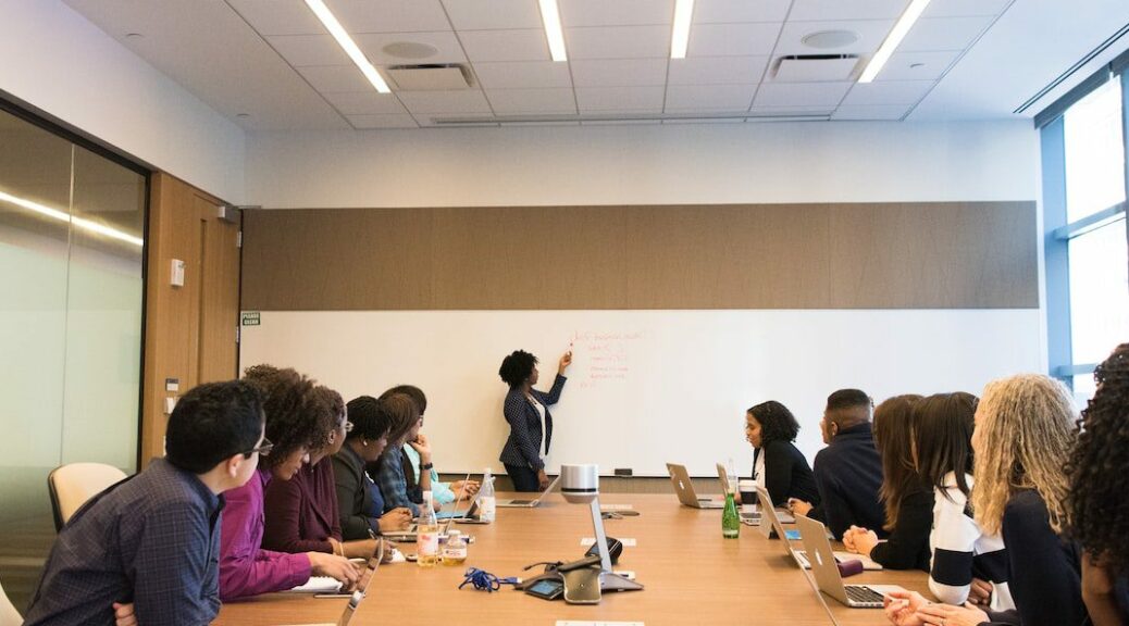 people on conference table looking at talking woman