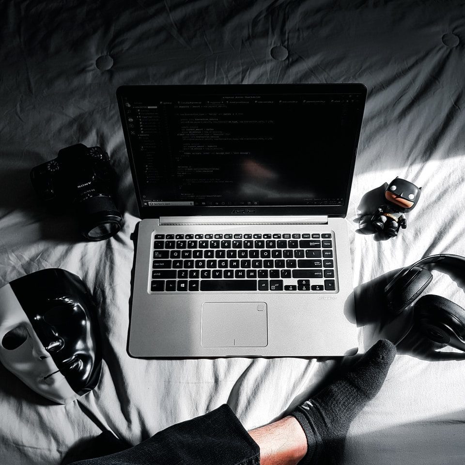 MacBook in middle of camera, action camera, mask, and headphones on bed