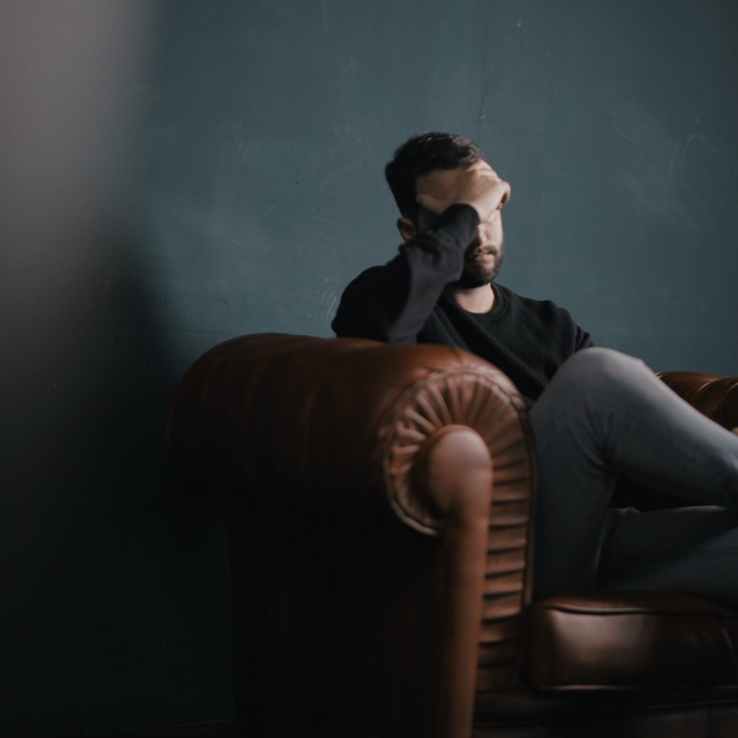 a man holds his head while sitting on a sofa