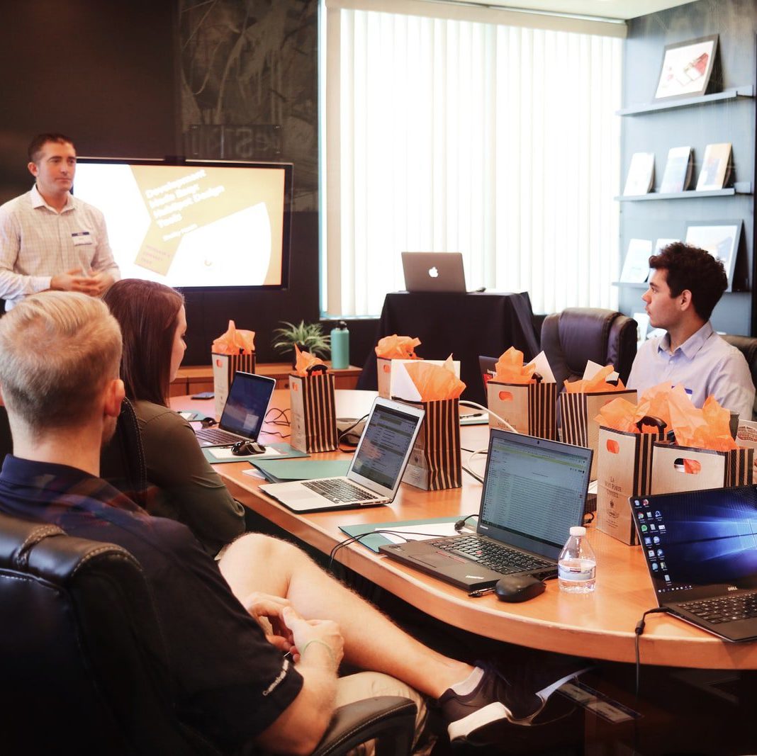 man standing in front of people sitting beside table with laptop computers